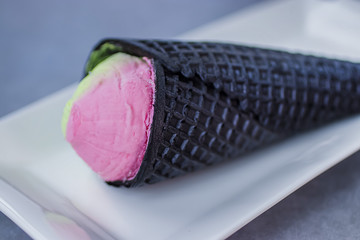 Bright pink-green ice cream in afashionable black cone.
