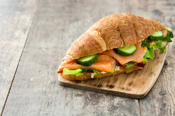 Croissant sandwich with salmon and vegetables on wooden table. Copyspace