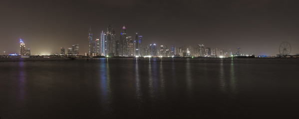 Skyscrapers of Dubai Marina at night. The lights of the modern buildings are reflected in the Persian Gulf sea in front of the buildings