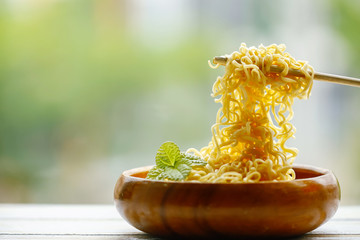 Instant noodle in wooden bowl with bamboo chopstick on green background