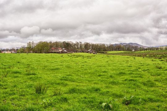 The view over the village of Drymen in Stirlingshire, Scotland, in spring time. Lavish green pasture in the foreground. Dramatic clouds