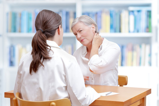 Senior female patient consulting her physician or doctor on account of chronic neck pain caused by fibromyalgia or a herniated disc.