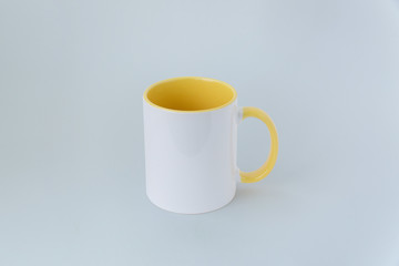A white mug, with a yellow handle on a gray background. 