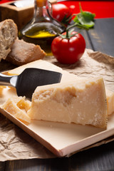Traditional italian food - aged Italian parmesan hard cheese Parmigiano-Reggiano with cheese knife, tomato, basil, olive oil