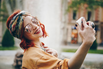 beautiful young woman wearing round sunglasses taking a selfie picture outdoors. hippie fashion...
