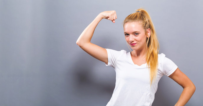 Powerful young fit woman flexing on a solid gray background