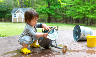 Toddler boy playing with a watering can outside © Tierney