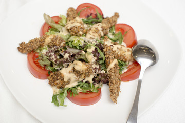 fried in a breaded chicken and fresh vegetable salad close-up on a plate on a white table. view from above.
