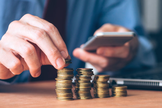 Businessman using smartphone with stacked coins in foreground