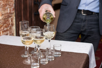 Male sommelier pouring white wine into long-stemmed wineglasses