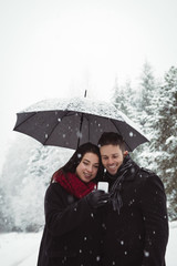 Smiling couple under umbrella using mobile phone in forest