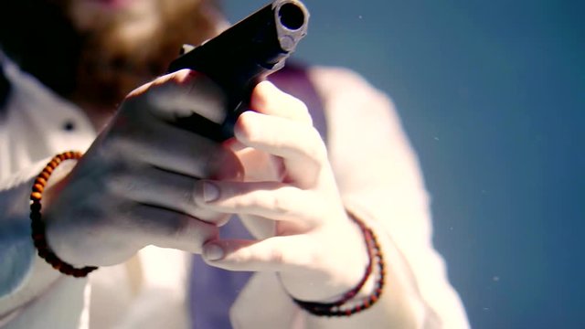 injured bearded man is sinking in clear water in pool, aiming by handgun and diving on bottom, close-up