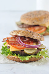 Hamburger with beef patties and fried bacon. The filling consists of a slice of cheese, pickled cucumber, tomato, lettuce, onions and sauce. Vertical orientation of the frame. Close-up.