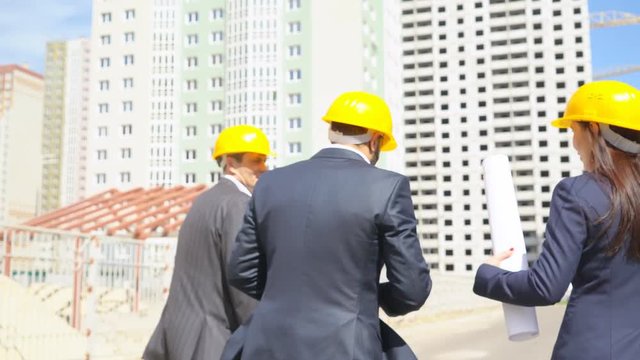 businessmen are going on construction and are considering a new project under construction. Serious people in suits in protective helmets of yellow color. 4k