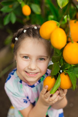 Fototapeta na wymiar Beautiful little happy girl in colorful dress in lemon garden Lemonarium picking fresh ripe lemons in her basket