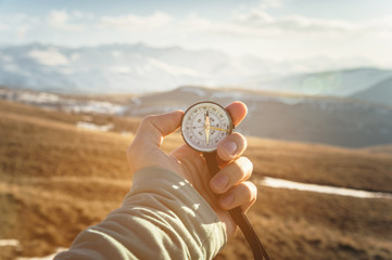 a man's hand holds a hand-held compass against the backdrop of mountains and hills at sunset. The concept of travel and navigation in open areas © yanik88