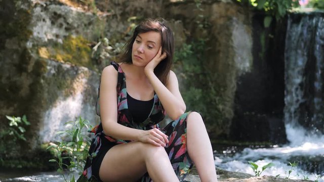 Thoughtful Lonely pretty caucasian woman near the waterfall