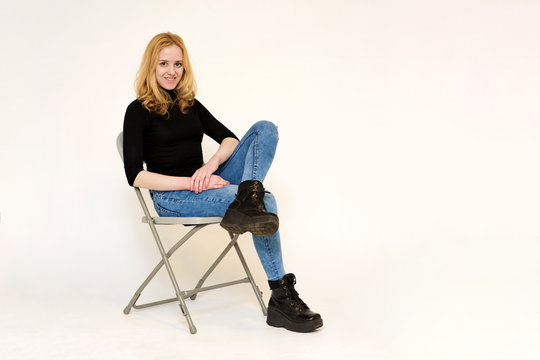 Portrait of a beautiful blonde girl in jeans sitting on a chair on a white background