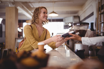 Smiling beautiful female customer paying through card at counter