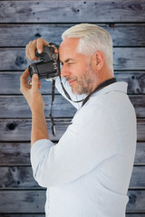 Smiling man taking a photo on digital camera against wooden background in blue