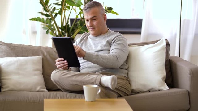 technology, online shopping, people and lifestyle concept - man with tablet pc computer and credit card sitting on sofa at home