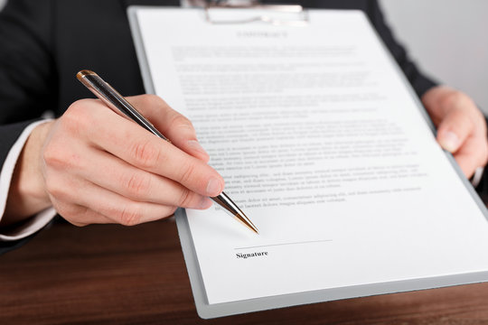 Close up of a businessman handing over a contract, attached to a clipboard for signature.