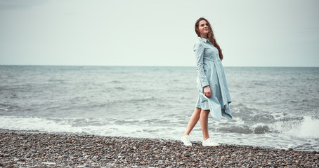 Girl on the coast. Lady on the sea. Attractive lady walks along the beach. Portrait of a girl on a background of the sea. She stands on the beach
