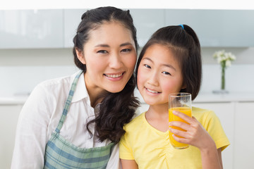 Girl holding orange juice with her mother in kitchen