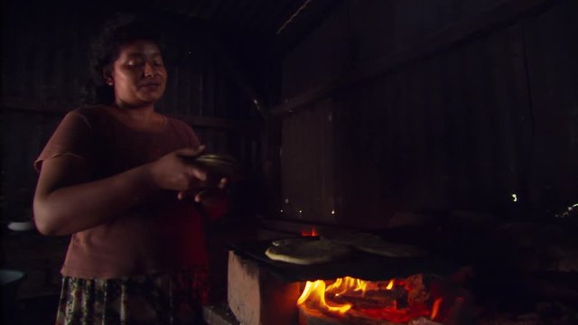 Woman cooking tortillas over fire in dim interior of Salvadoran home