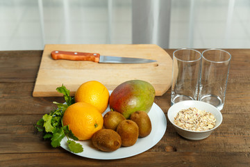 on a wooden table on a white plate lie the mango oranges kiwi fruit. Nearby are two glasses and a...