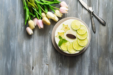 Appetizing cake with slices of lime and mint with tulips on a wooden gray background.