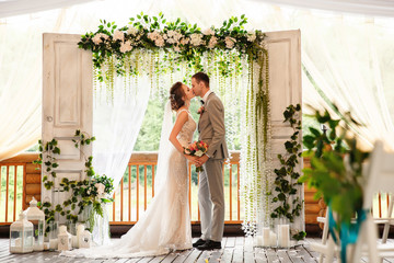 Wedding ceremony. Elegant wedding couple kissing near wedding arch, bride and groom in love