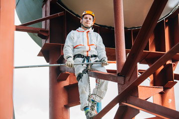 Industrial climber in helmet and uniform painting water tower. Professional Painter working on...