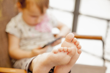 Fototapeta premium The little child girl holding a mobile phone in his hands and resting on the ship while traveling. Selective focus on the legs.