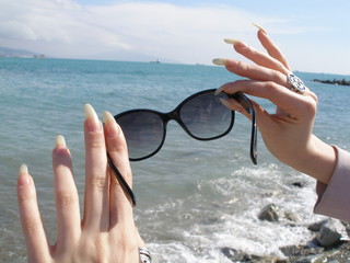 Woman hands with long finger nails with sunglasses sea view