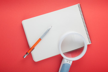 Top view on blank paper notepad, pencil and magnifier