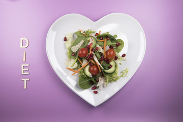 Traditional salad on a heart shaped plate with the word diet in wooden letters 