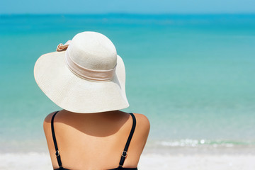 Happy woman enjoying beach relaxing joyful in summer by tropical blue water. Beautiful bikini model happy on travel wearing beach sun hat on beach. Girl on a tropical beach with hat