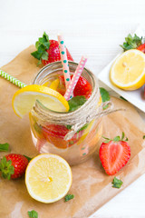 Mineral  water with fresh strawberries, lemon  and mint in jar on a white wooden background, copy space