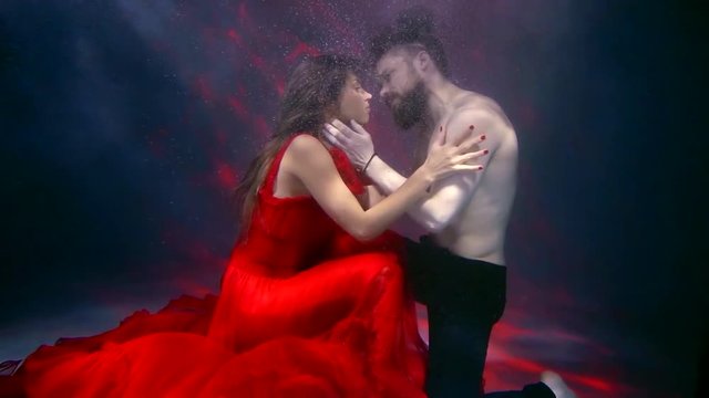 underwater shot of sad young man is trying to embrace pretty woman in red dress, but she is leaving him and swimming away