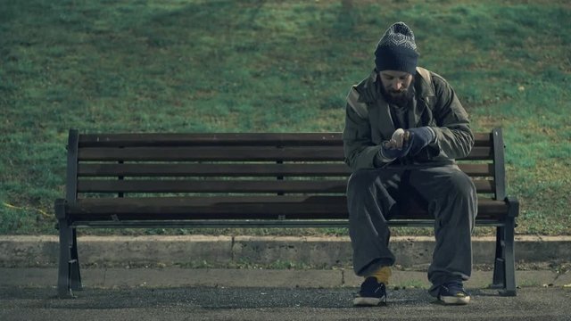 Lonely beggar on bench cheking his money