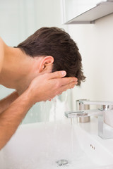 Shirtless young man washing face in bathroom