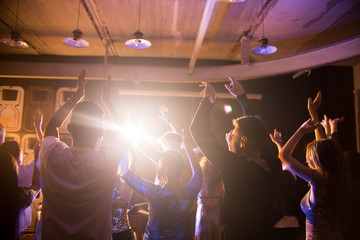 Back view at crowd of trendy young people dancing in nightclub and enjoying party, focus on beautiful women wearing glittering tops on dance floor