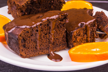 Pieces of chocolate cake poured with chocolate on a white plate and orange slices