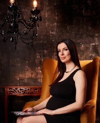 Pregnant woman in elegant dress sitting in lobby