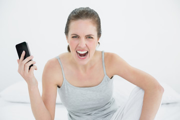 Angry woman shouting with mobile phone in hand on bed