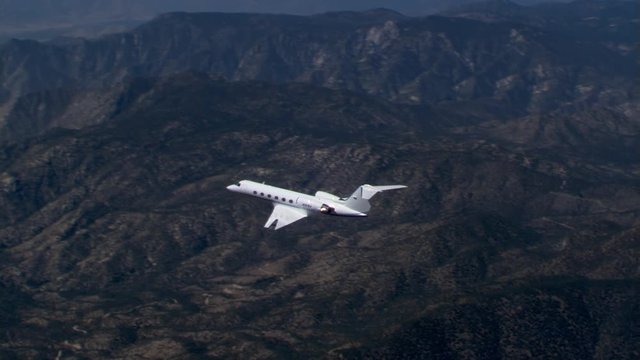 Air-to-air side view of executive jet over rugged terrain