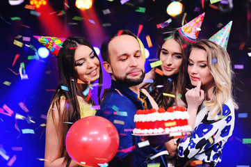 a young man in the company of friends makes a wish blowing out their candles on the cake