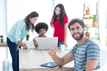 Casual businessman using digital tablet with colleagues behind in office