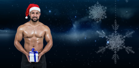 Muscular man in santa hat against snowflakes hanging against starry sky